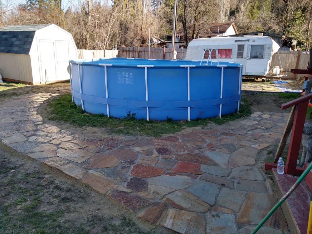 Flagstone patio laid around an above-ground pool in a back yard