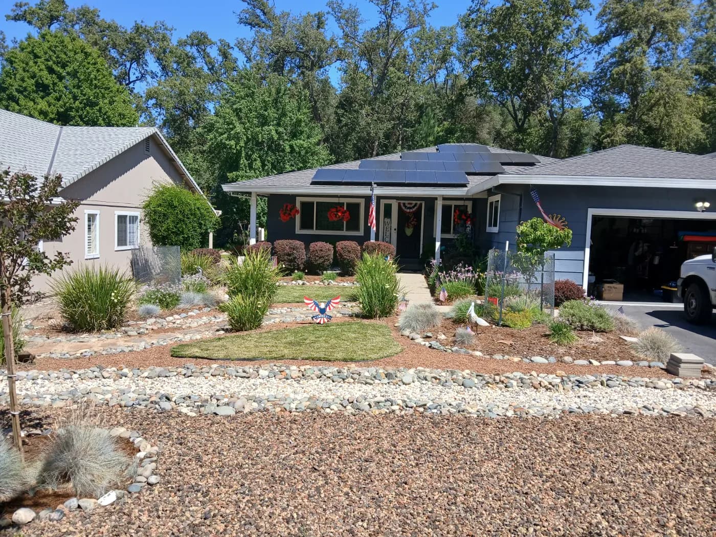 Front yard planted with ornamental grasses and shrubs between river rock swales and gravel at a foothill home