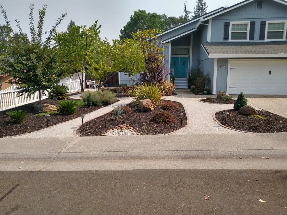 Decomposed granite paths curving between mulched beds, boulders, and path lighting in a front yard